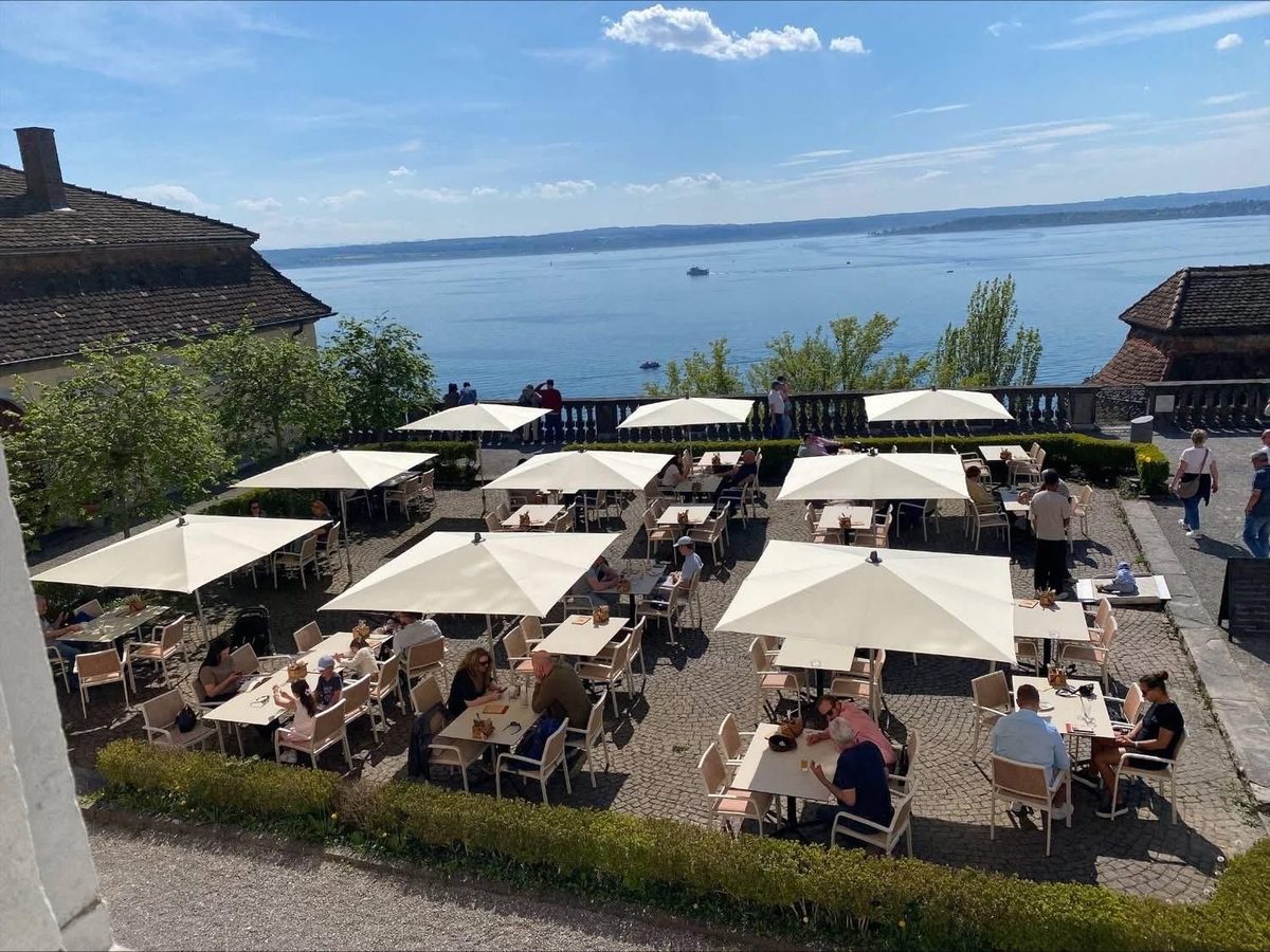Terrazza sul lago con ombrelloni color crema, tavoli e sedie chiare