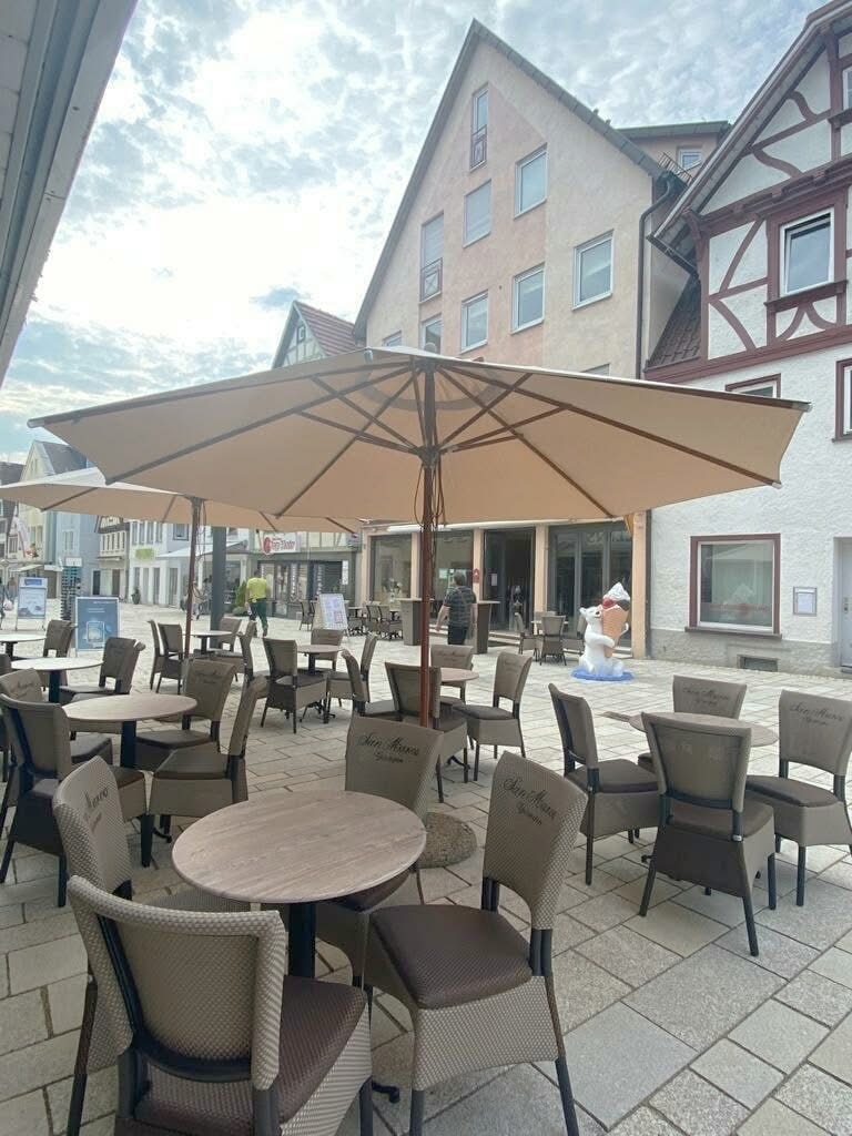 Piazza pedonale con tavolini rotondi, poltroncine intrecciate color tortora e grande ombrellone